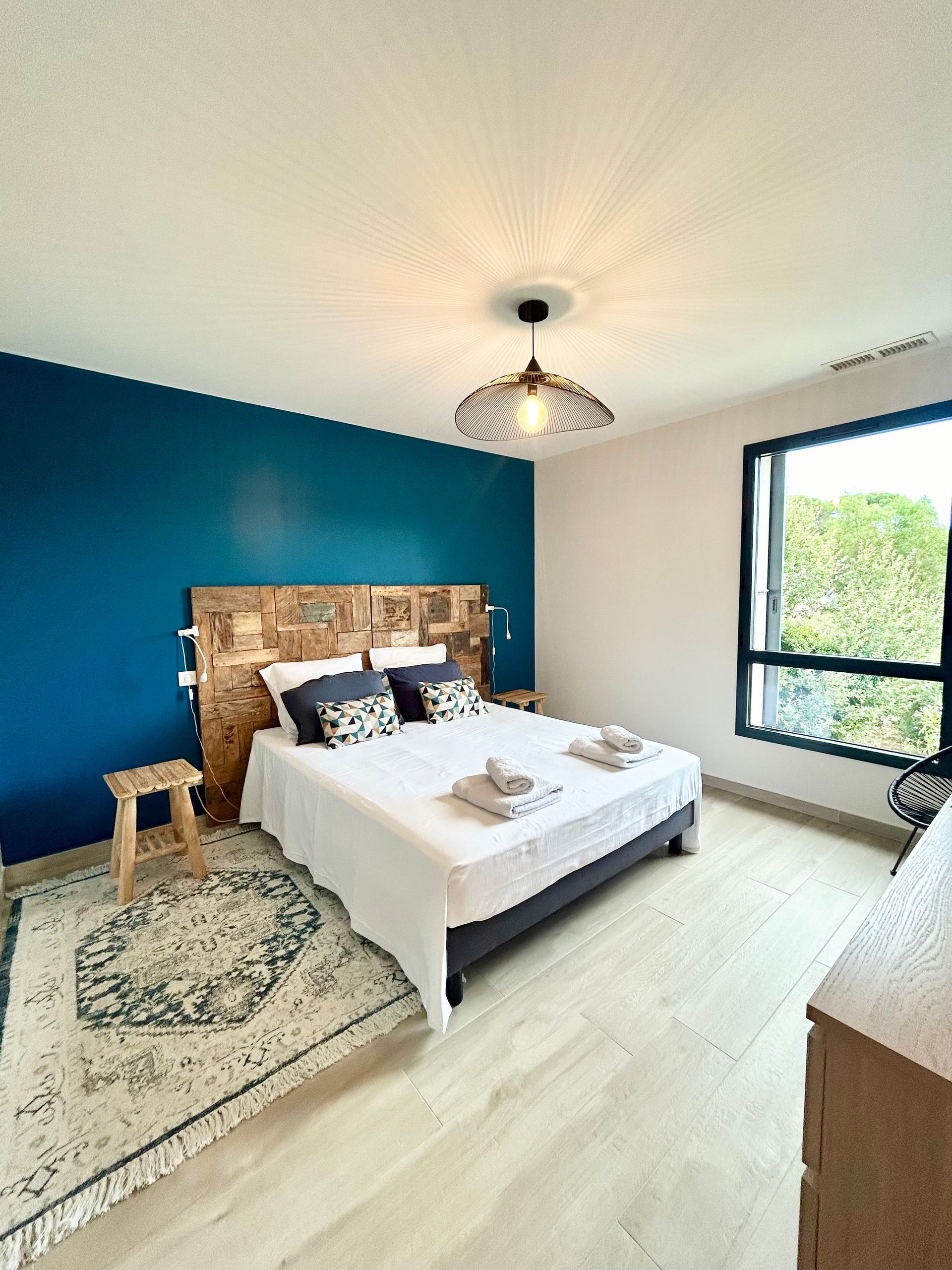 Chambre avec un mur d'accent bleu, une tête de lit en bois, du linge de lit blanc, un tapis et une fenêtre.