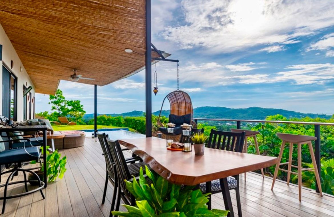 Terrasse avec table et chaises donnant sur un paysage verdoyant et un ciel bleu.