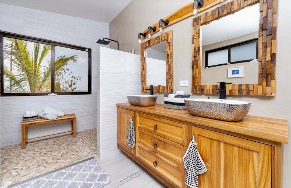 Salle de bains avec meuble-lavabo en bois, deux lavabos, miroirs et douche. Fenêtre avec vue sur l'extérieur.