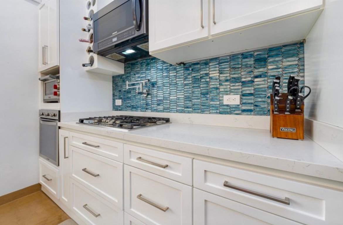 Cuisine blanche avec crédence en carrelage bleu, plaque de cuisson au gaz et plans de travail blancs.