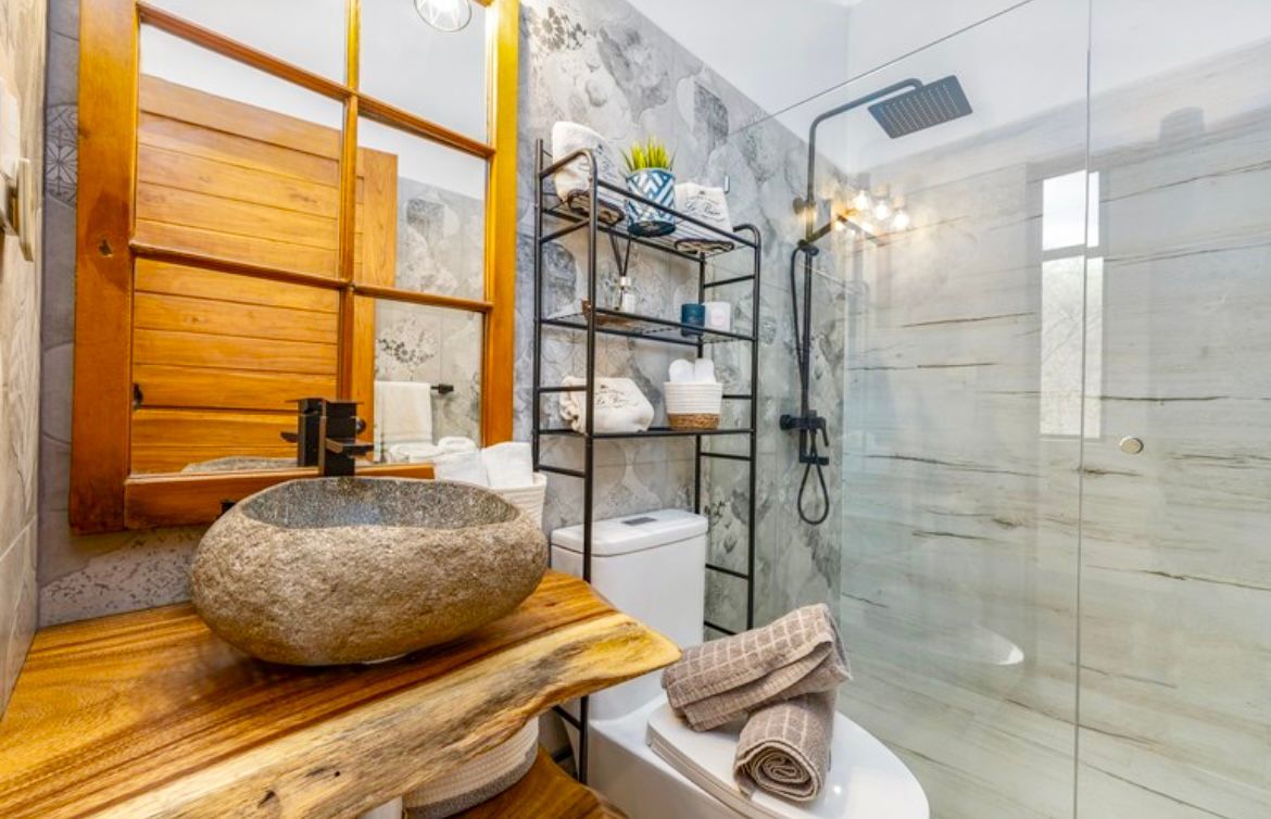 Salle de bains avec lavabo en pierre, éléments en bois, douche en verre et étagères en métal.