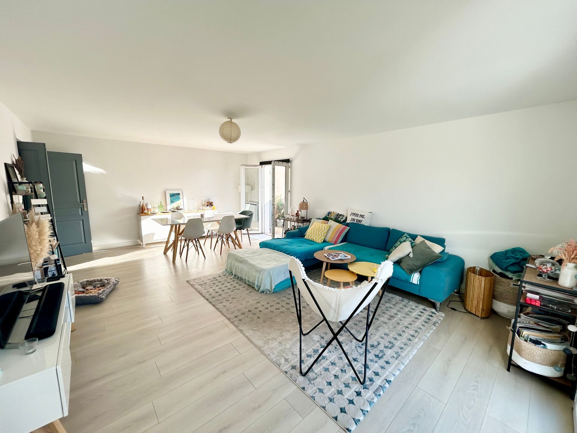 Salon lumineux avec canapé bleu, murs blancs, coin repas et parquet clair.