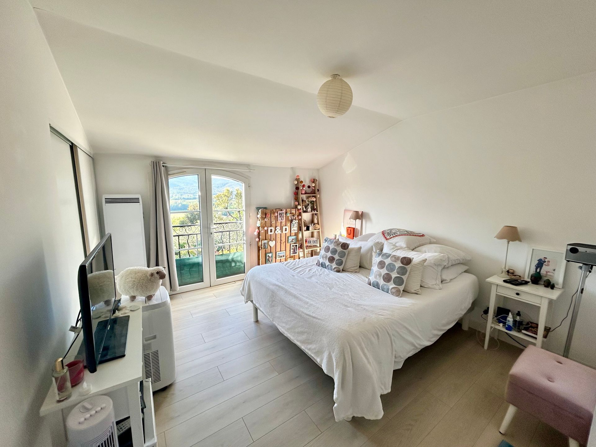 Chambre avec un lit blanc, des petites tables et un balcon donnant sur de la verdure.