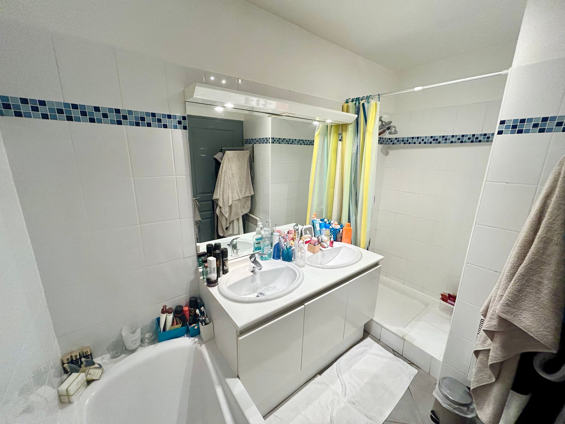 Salle de bains avec carrelage blanc et bleu, double vasque, miroir, douche et baignoire.