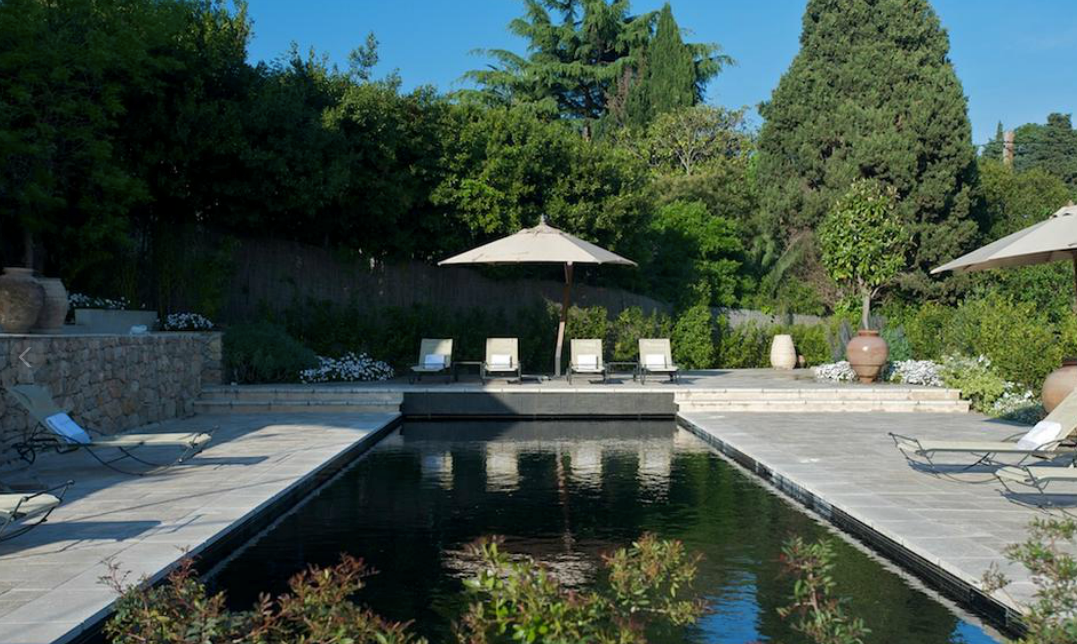Espace piscine avec chaises longues, parasols et végétation luxuriante.
