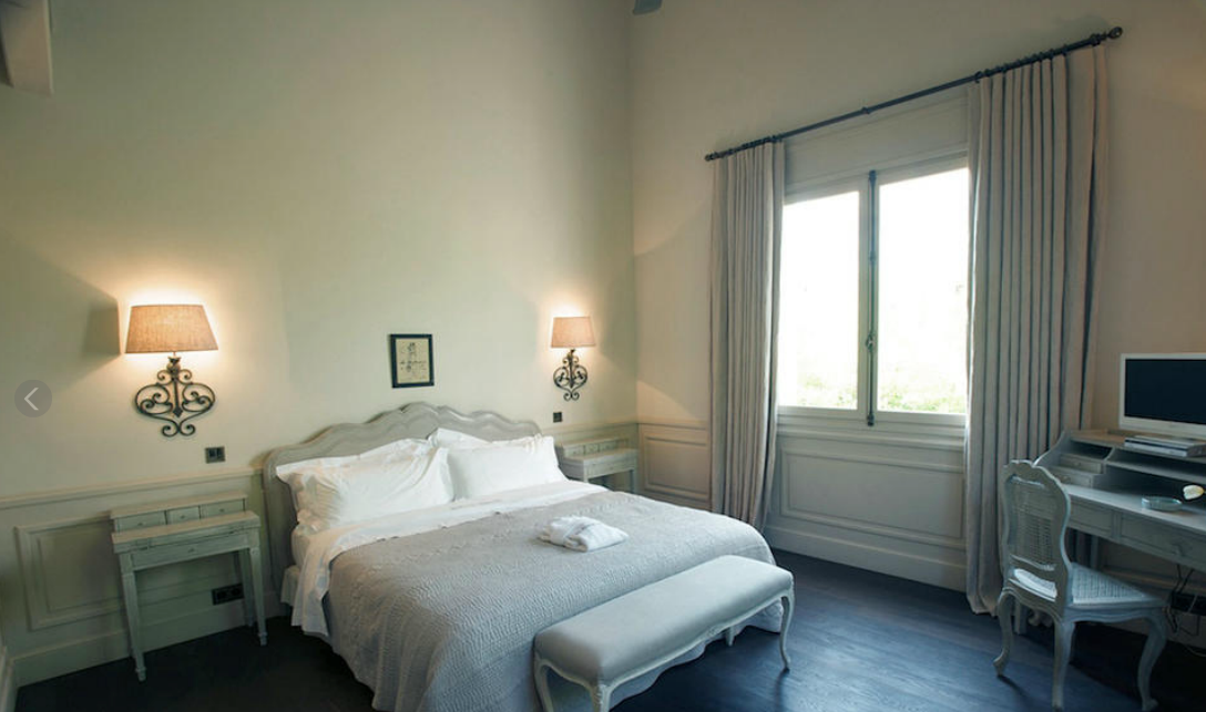 Chambre avec lit, tables de chevet, bureau, fenêtre et appliques murales.