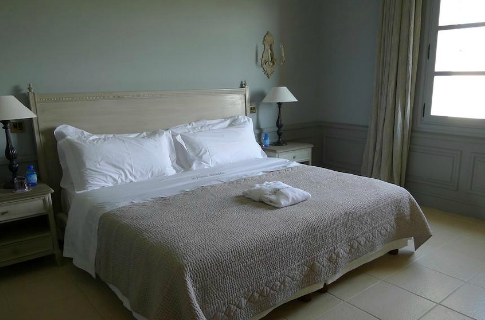 Chambre avec un lit blanc, un couvre-lit beige, des tables de chevet, des lampes et une fenêtre.