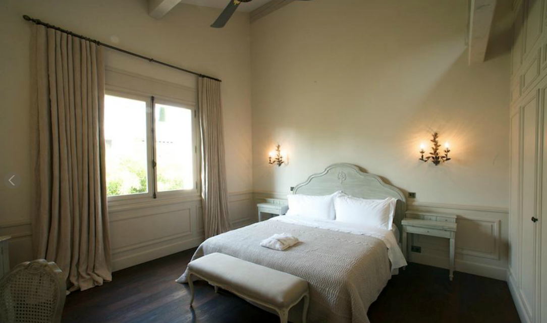 Chambre avec un lit double, des tables de chevet et une grande fenêtre avec des rideaux beiges.
