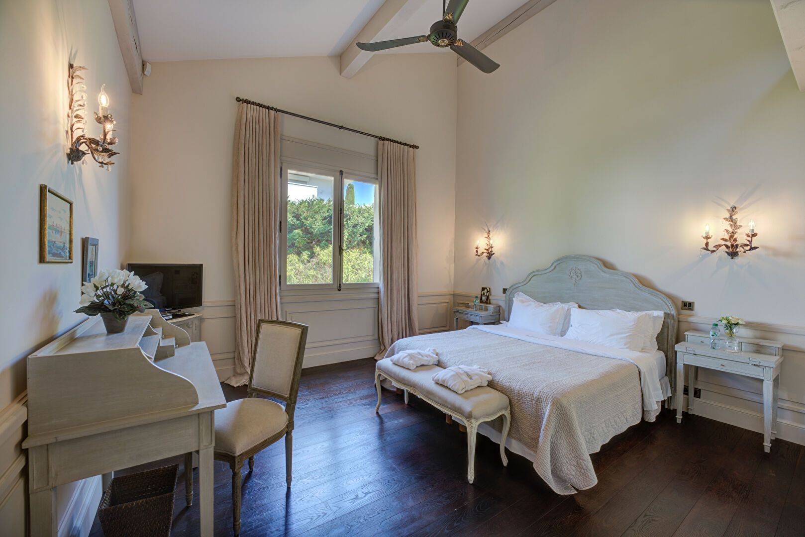 Chambre avec lit, coiffeuse, fenêtre avec vue et appliques murales.