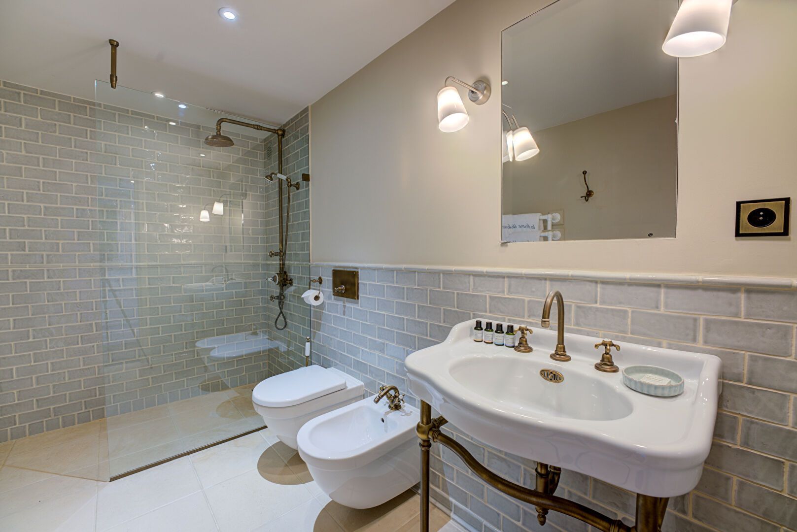 Salle de bains avec douche en verre, lavabo, toilettes, bidet et carrelage gris à motifs.