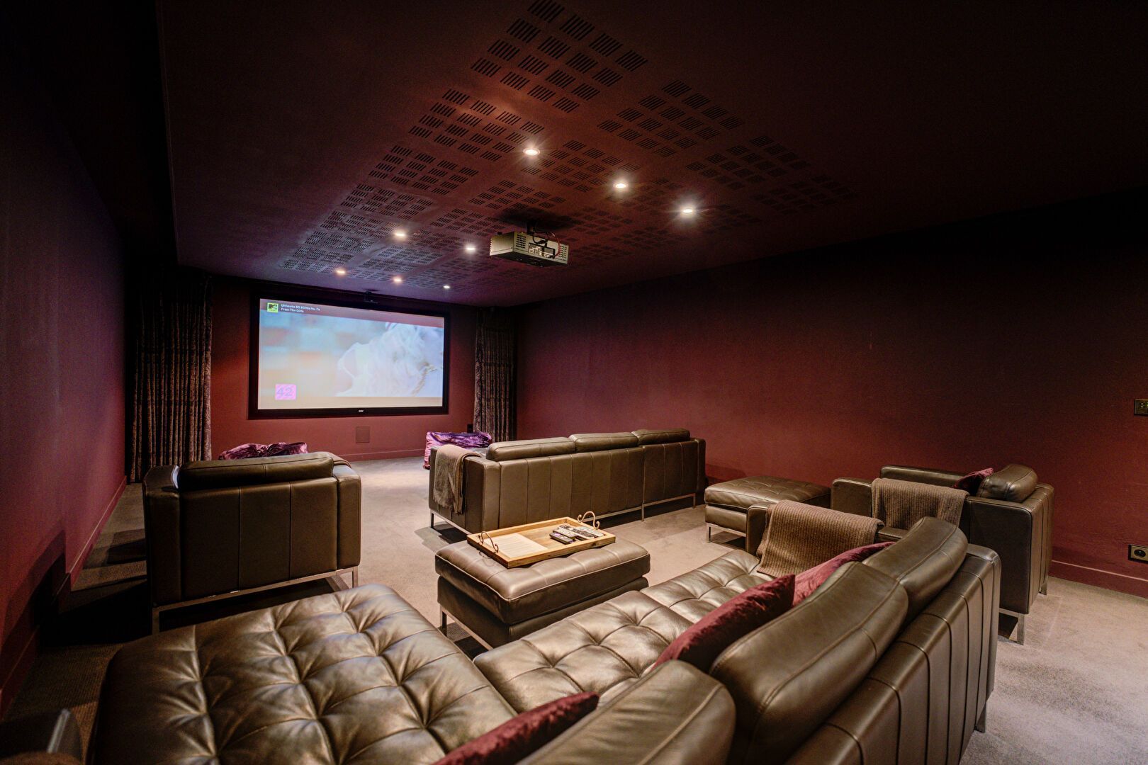 Salle de cinéma maison avec murs bordeaux, canapés en cuir et écran de projection.