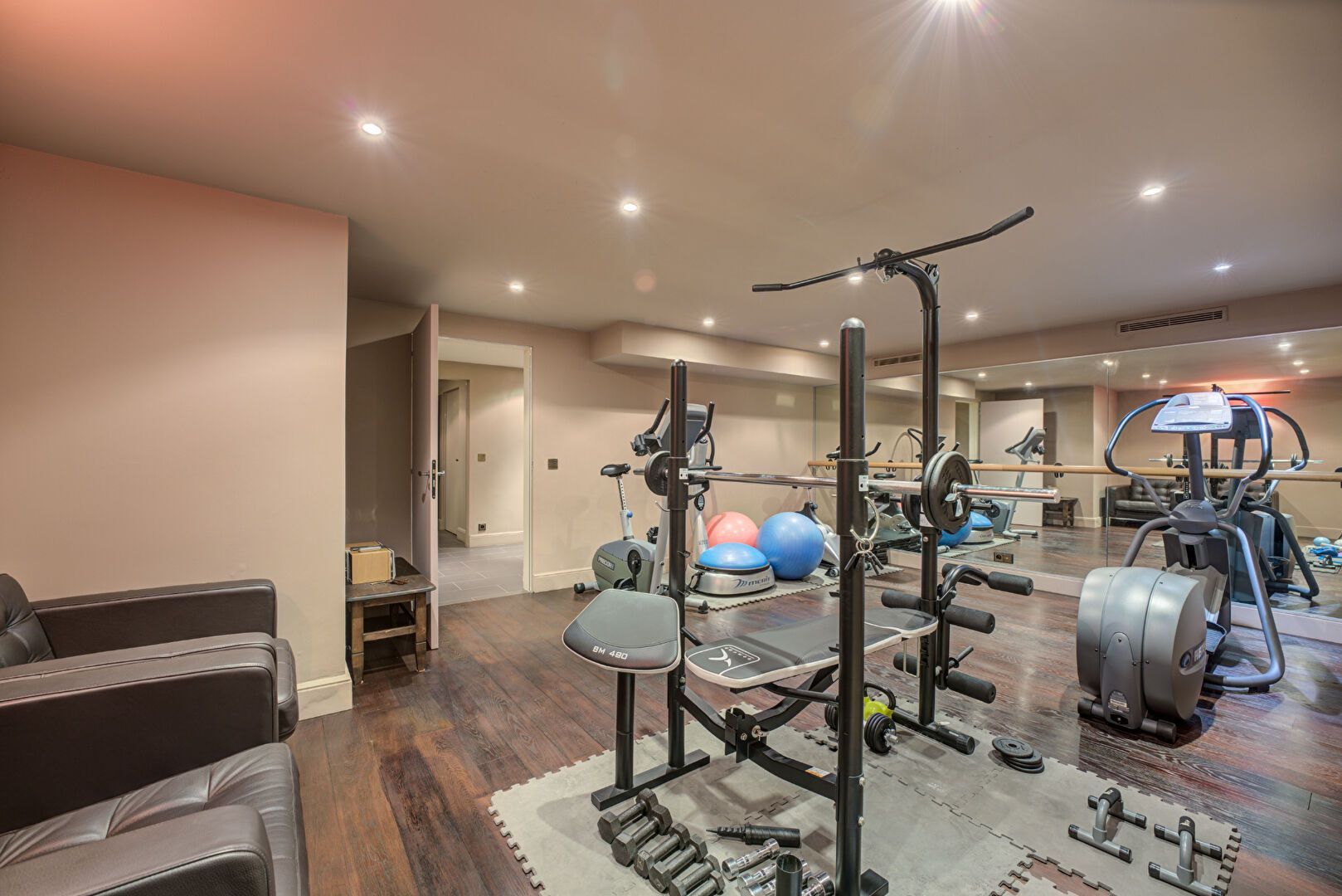 Salle de sport à domicile avec équipements de fitness sur parquet, murs aux couleurs neutres et éclairage lumineux.