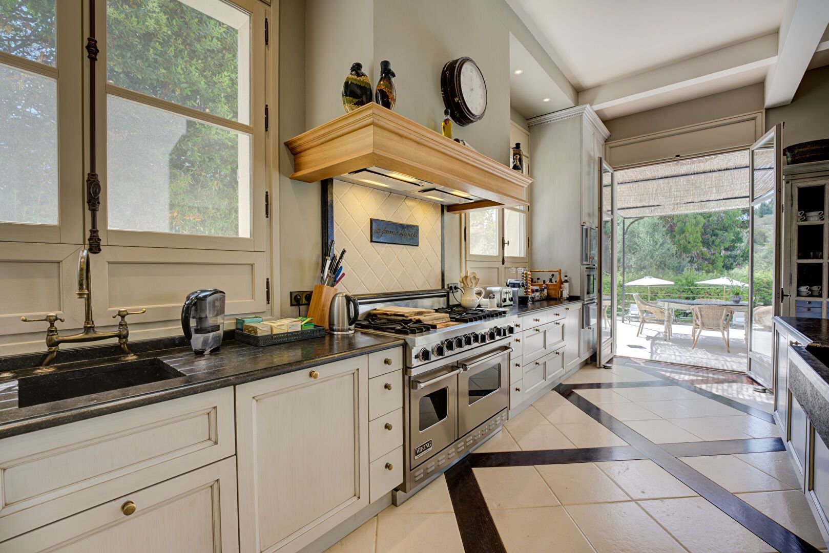 Cuisine élégante avec appareils électroménagers en acier inoxydable, sol en marbre et portes donnant sur un patio.