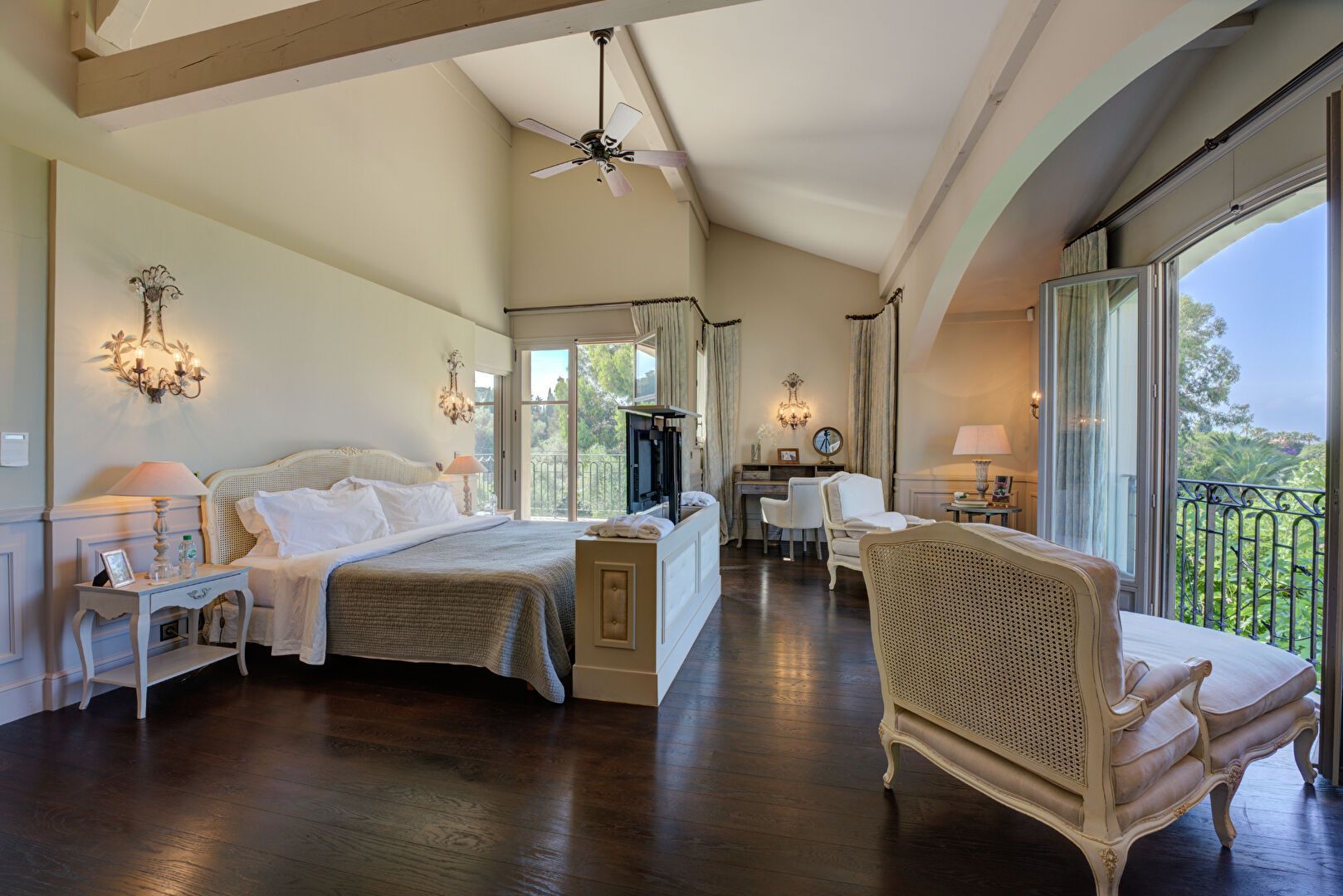 Chambre spacieuse avec parquet foncé, meubles blancs, balcon et hauts plafonds laissant entrer la lumière naturelle.