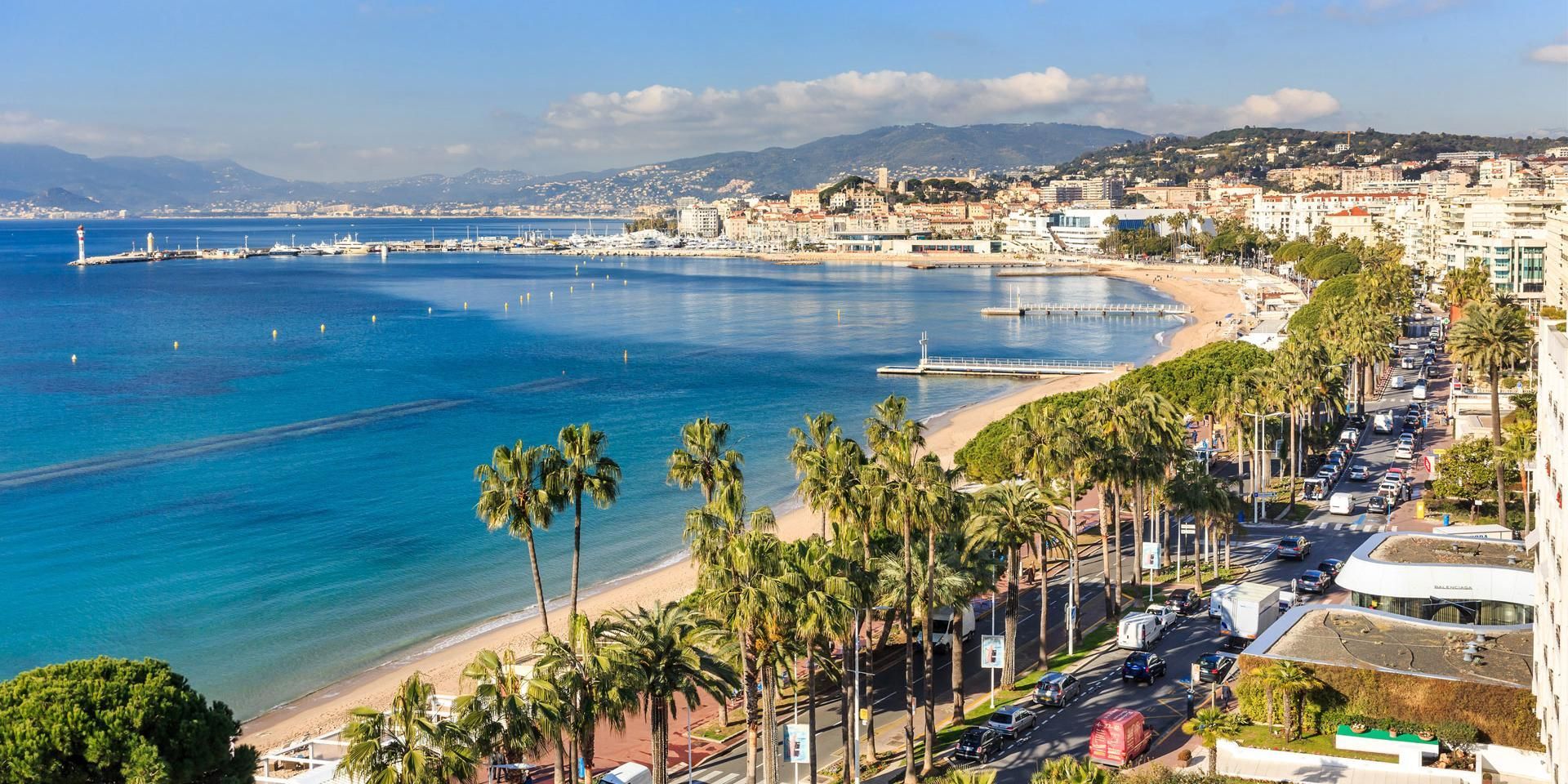 Paysage urbain côtier avec eau bleue, plage, palmiers et bâtiments.