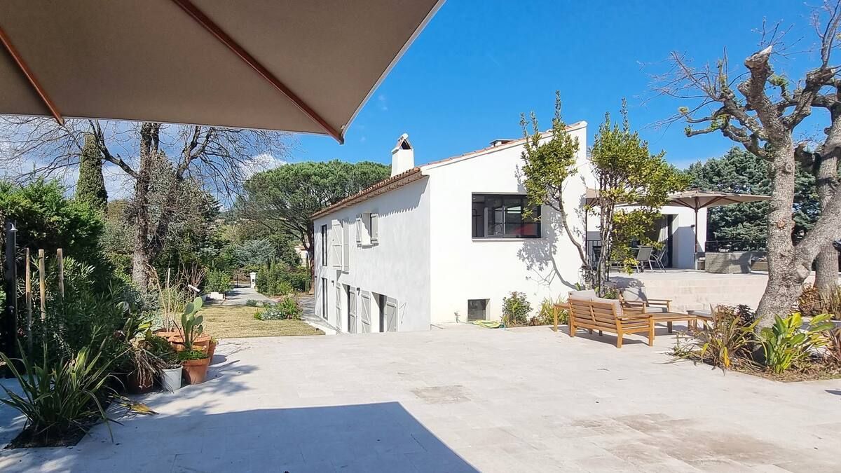 Maison blanche avec une cour intérieure, un parasol marron à gauche et un ciel bleu en arrière-plan.
