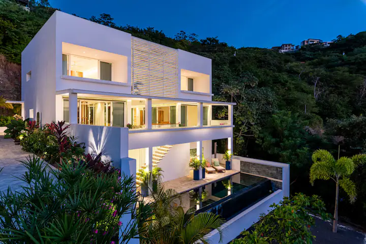 Maison blanche moderne avec piscine, adossée à une colline verdoyante.