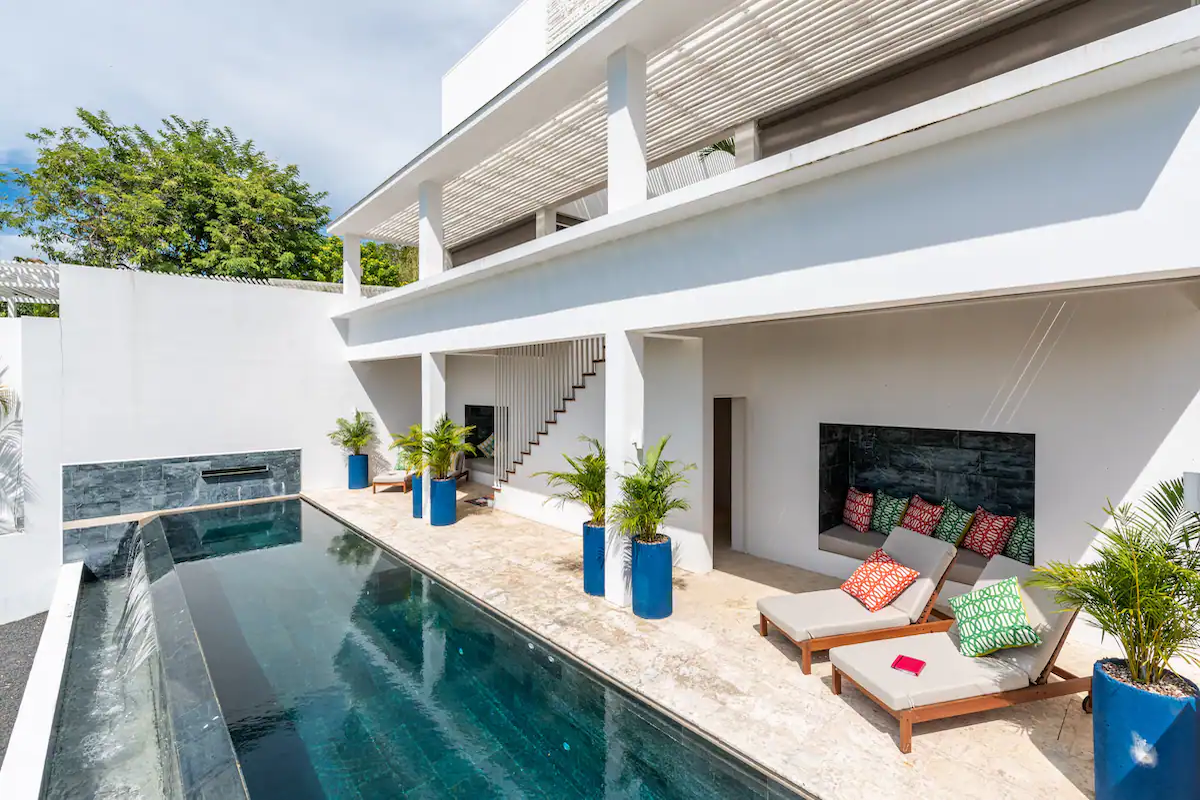 Vue depuis la piscine d'un bâtiment moderne blanc avec piscine, chaises longues et plantes en pot.