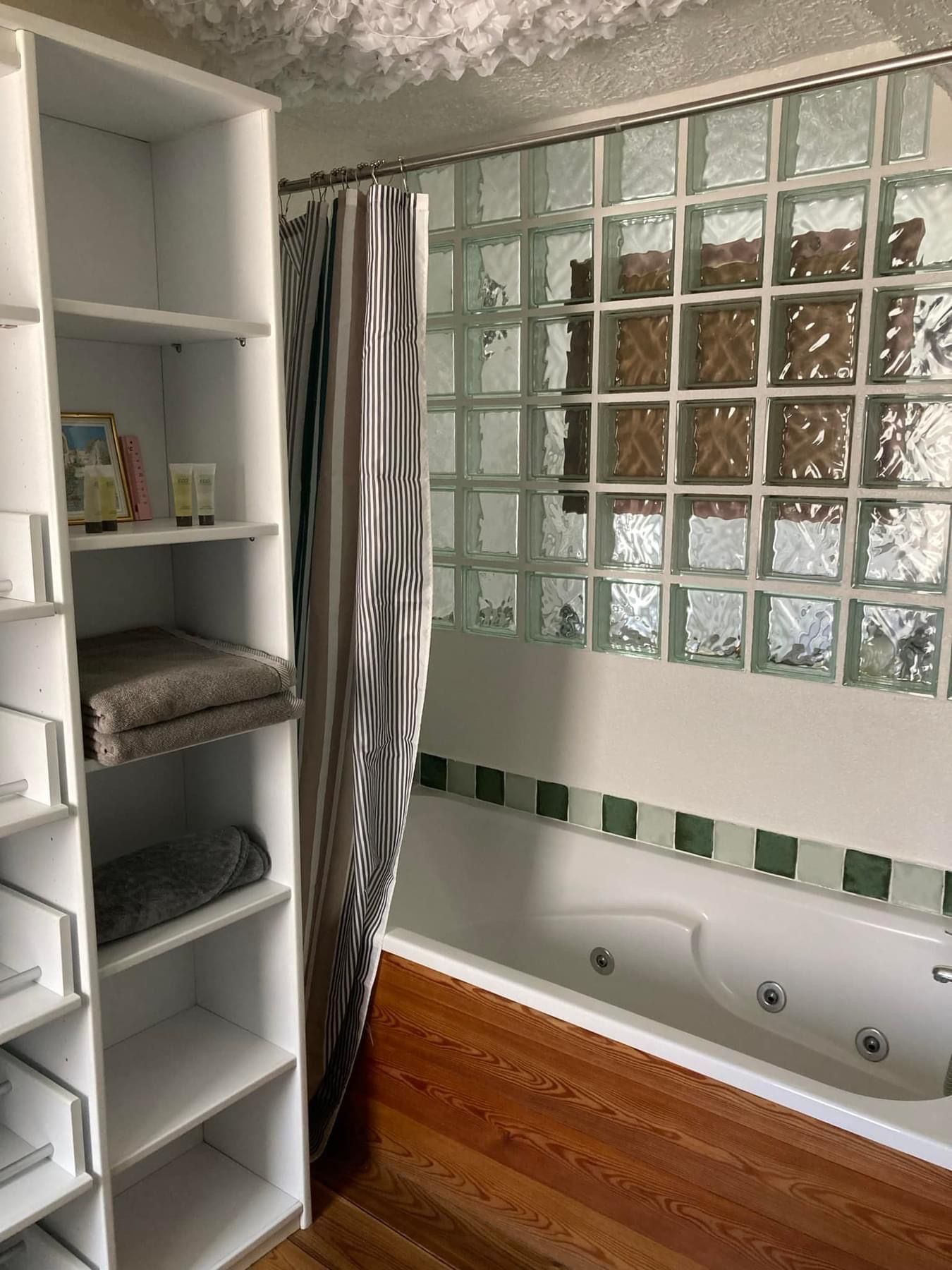 Salle de bains avec meuble blanc, douche, baignoire avec paroi en pavés de verre et sol en bois.