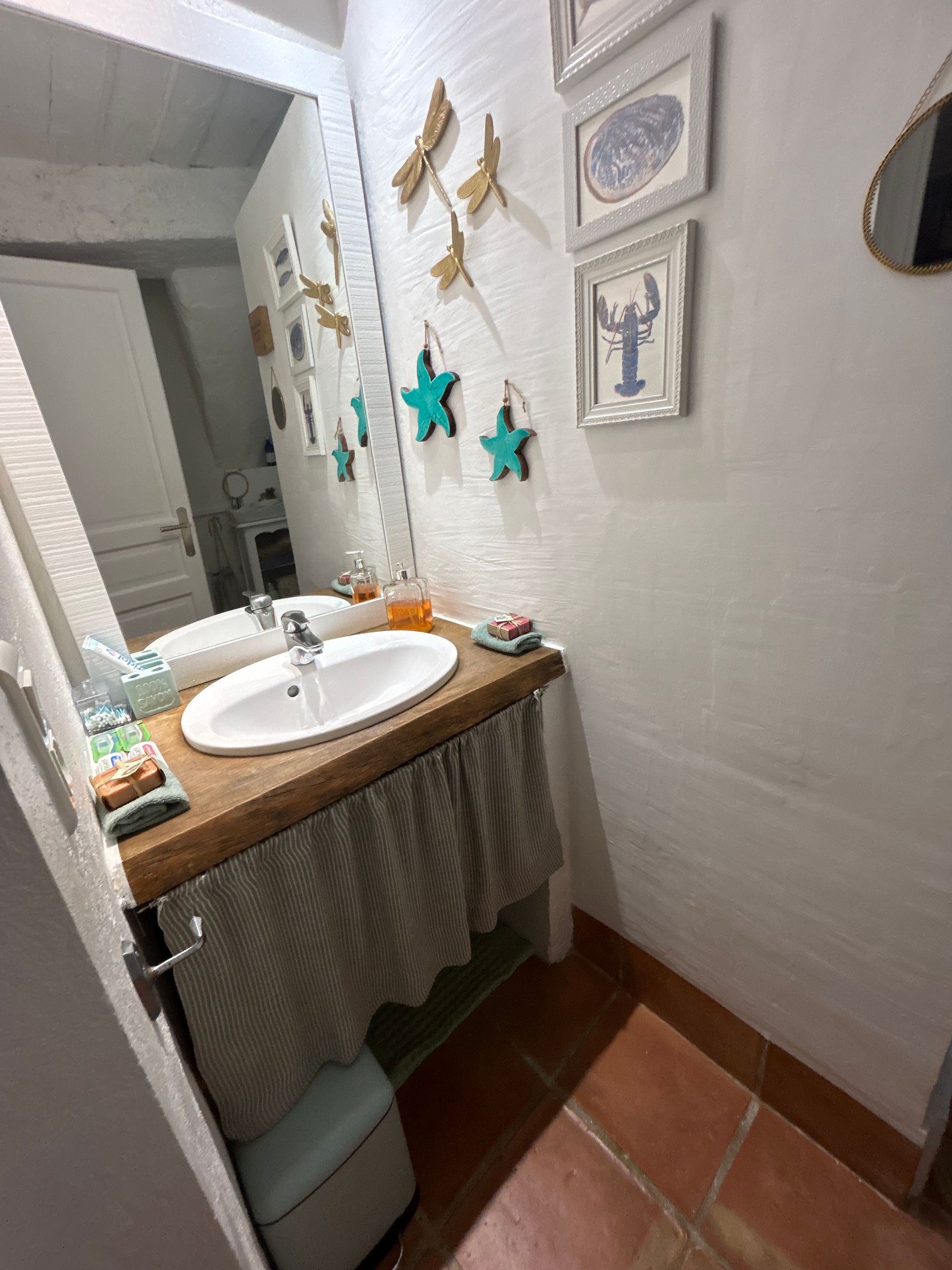 Salle de bains avec murs blancs, lavabo avec comptoir en bois et décorations murales.