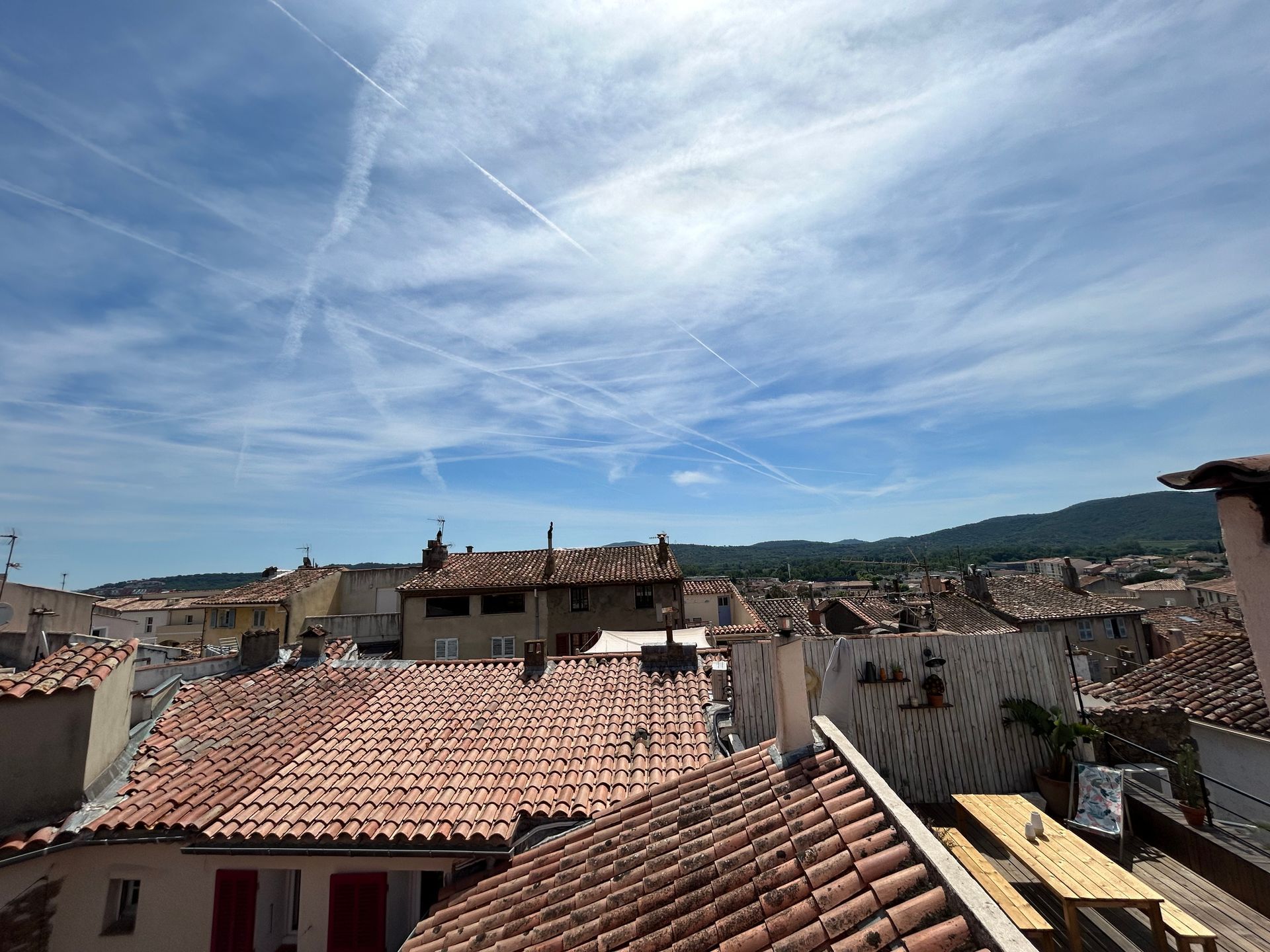 Toits d'immeubles sous un ciel d'un bleu éclatant, striés de traînées de condensation. Chaîne de montagnes visible au loin.