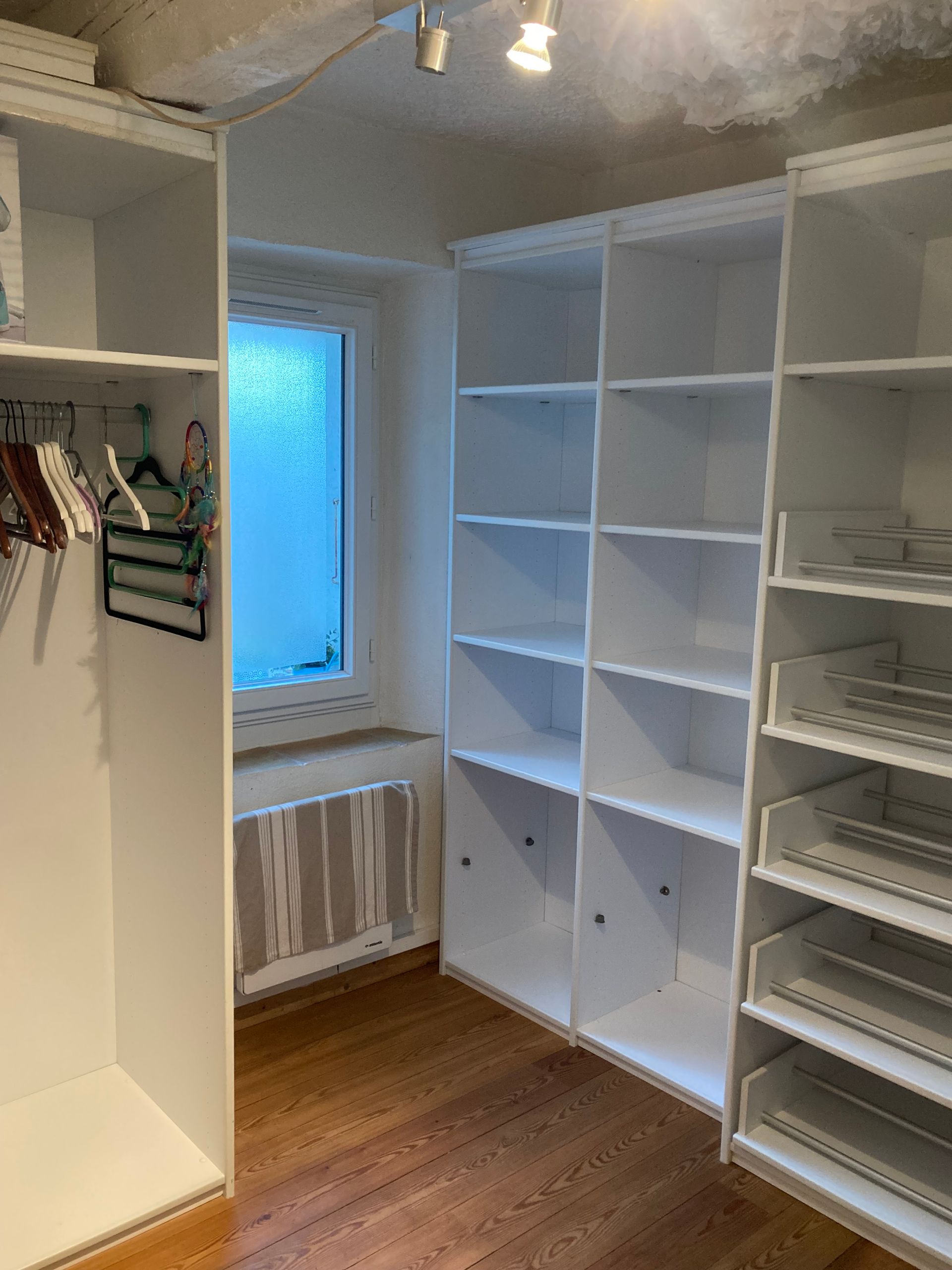 Dressing blanc avec étagères, tiroirs et fenêtre. Sol en bois et plafond en béton.