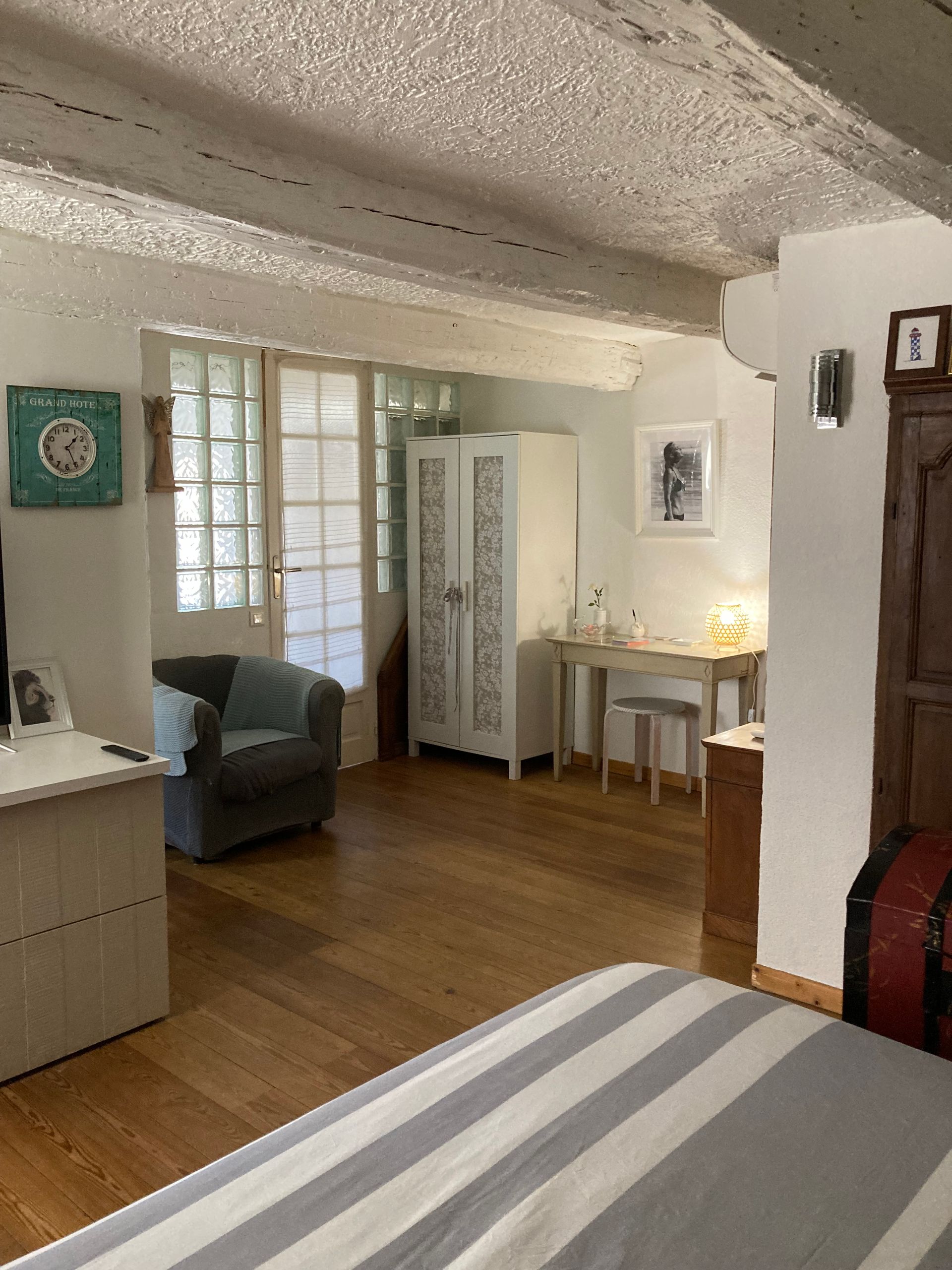 Intérieur de chambre avec parquet, poutres blanches, meubles et lit à rayures.