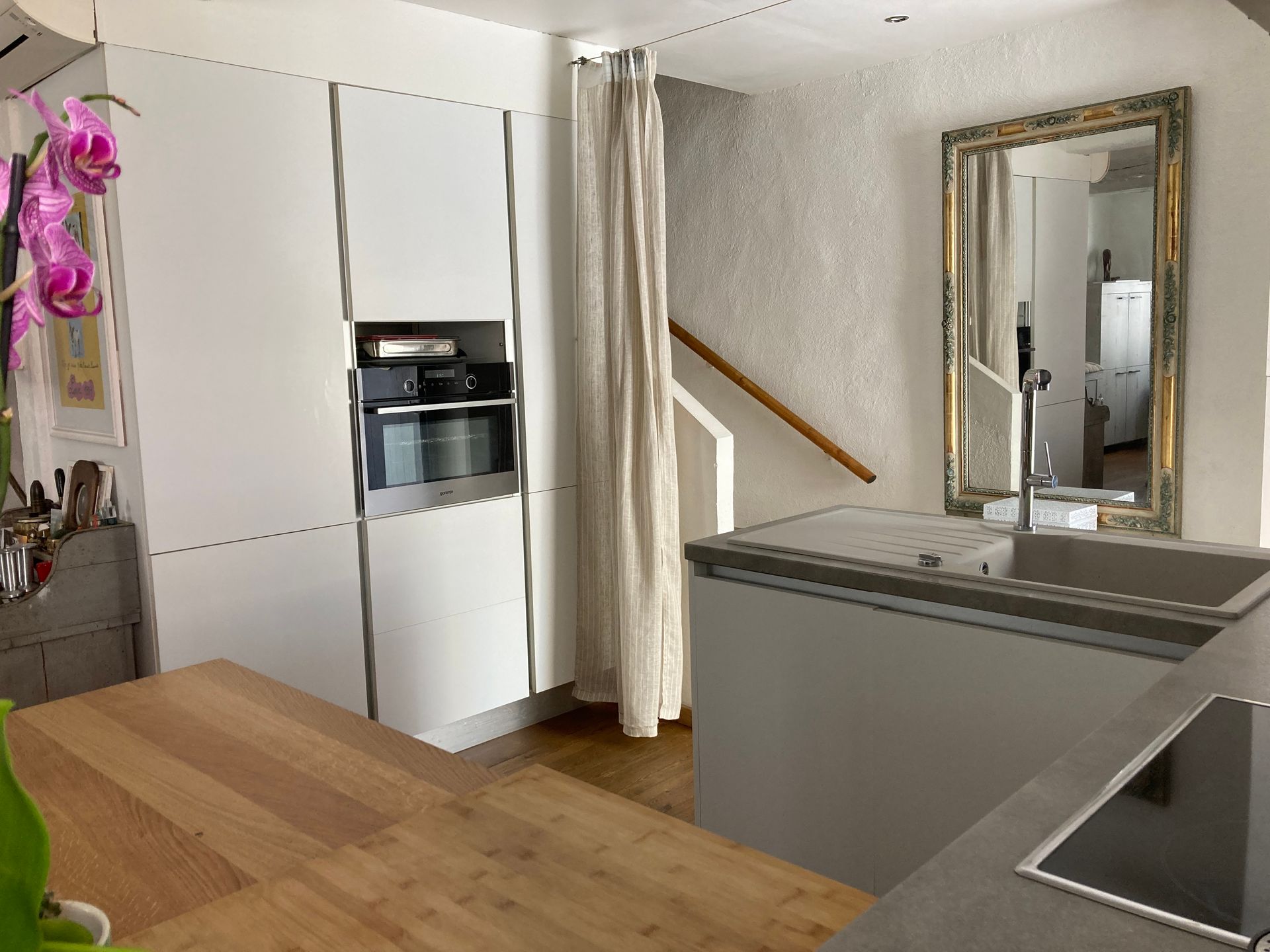 Cuisine moderne avec placards blancs, électroménager intégré, plan de travail en bois et miroir.