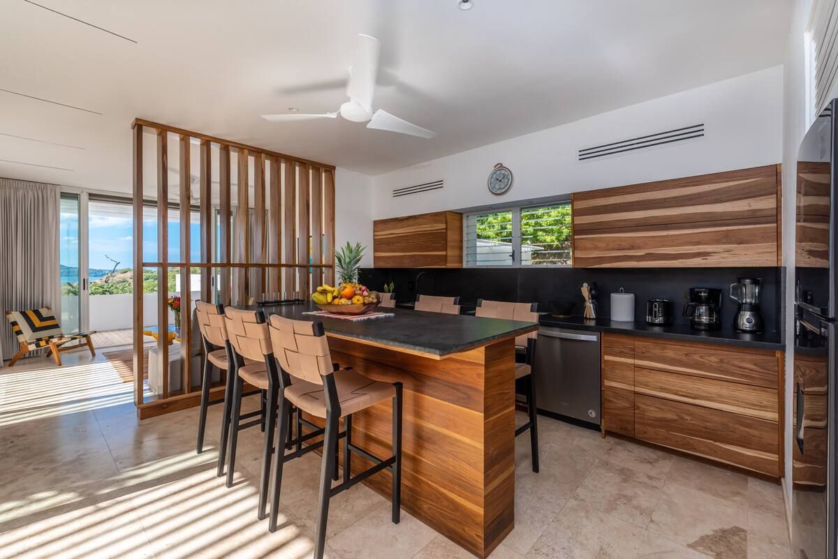 Cuisine moderne avec placards en bois, îlot central avec tabourets de bar et vue sur l'océan.