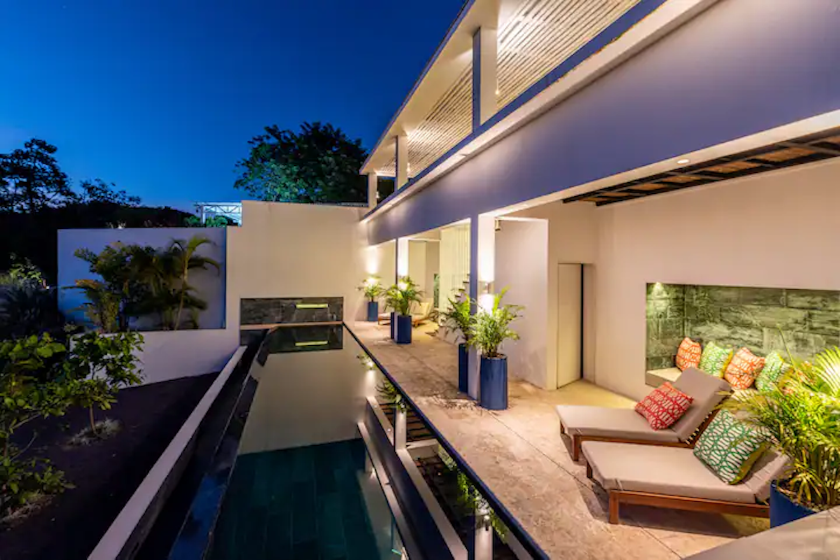Villa moderne avec piscine, chaises longues et éclairage nocturne.