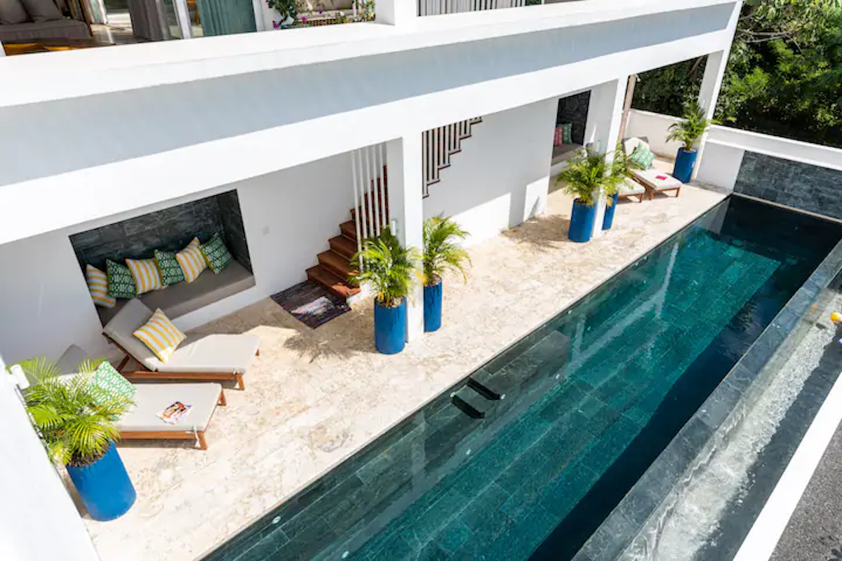 Bâtiment blanc moderne avec une longue piscine. Plantes tropicales en pots bleus, chaises longues et escalier.
