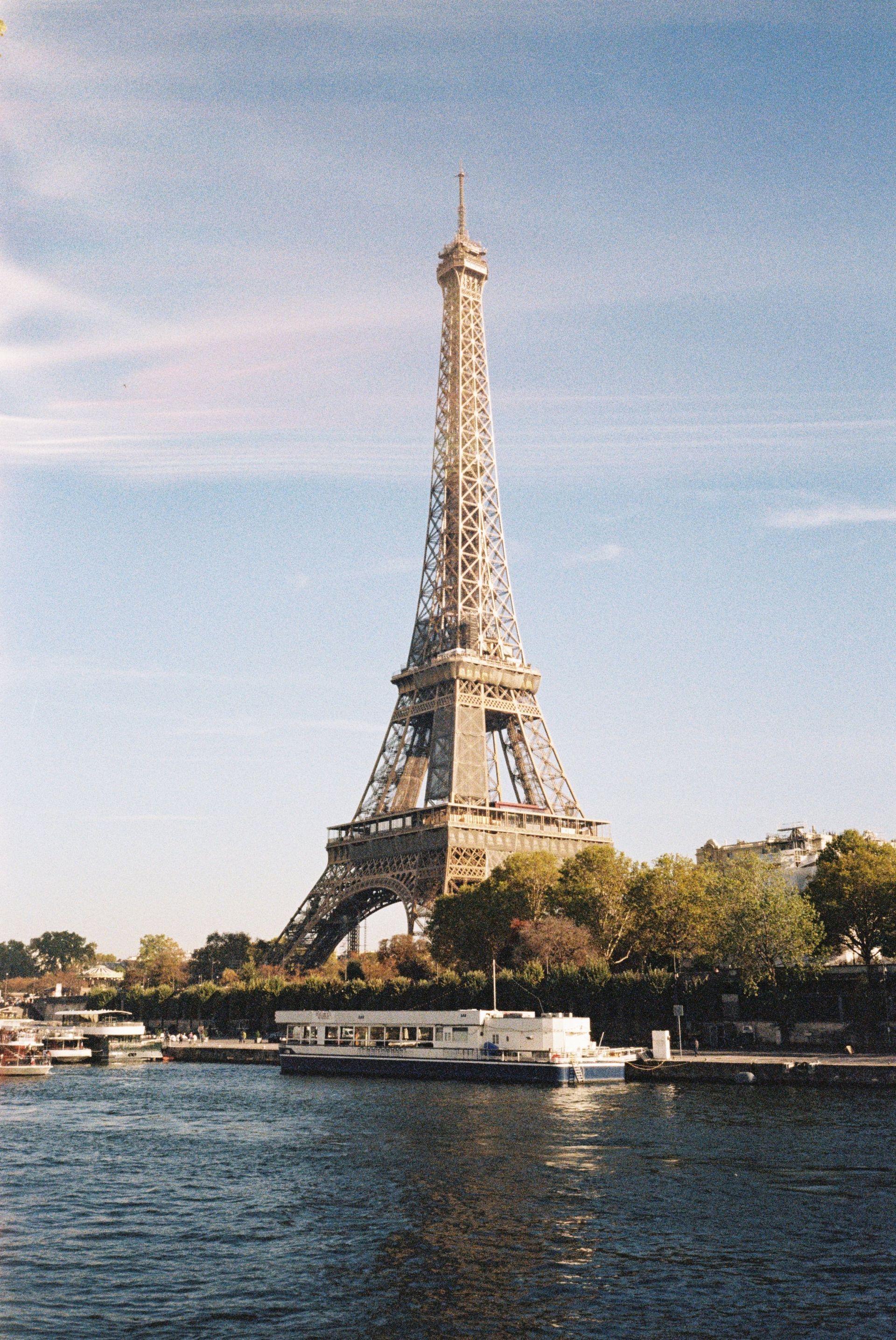 La tour Eiffel par une journée ensoleillée, au bord d'une rivière avec un bateau.