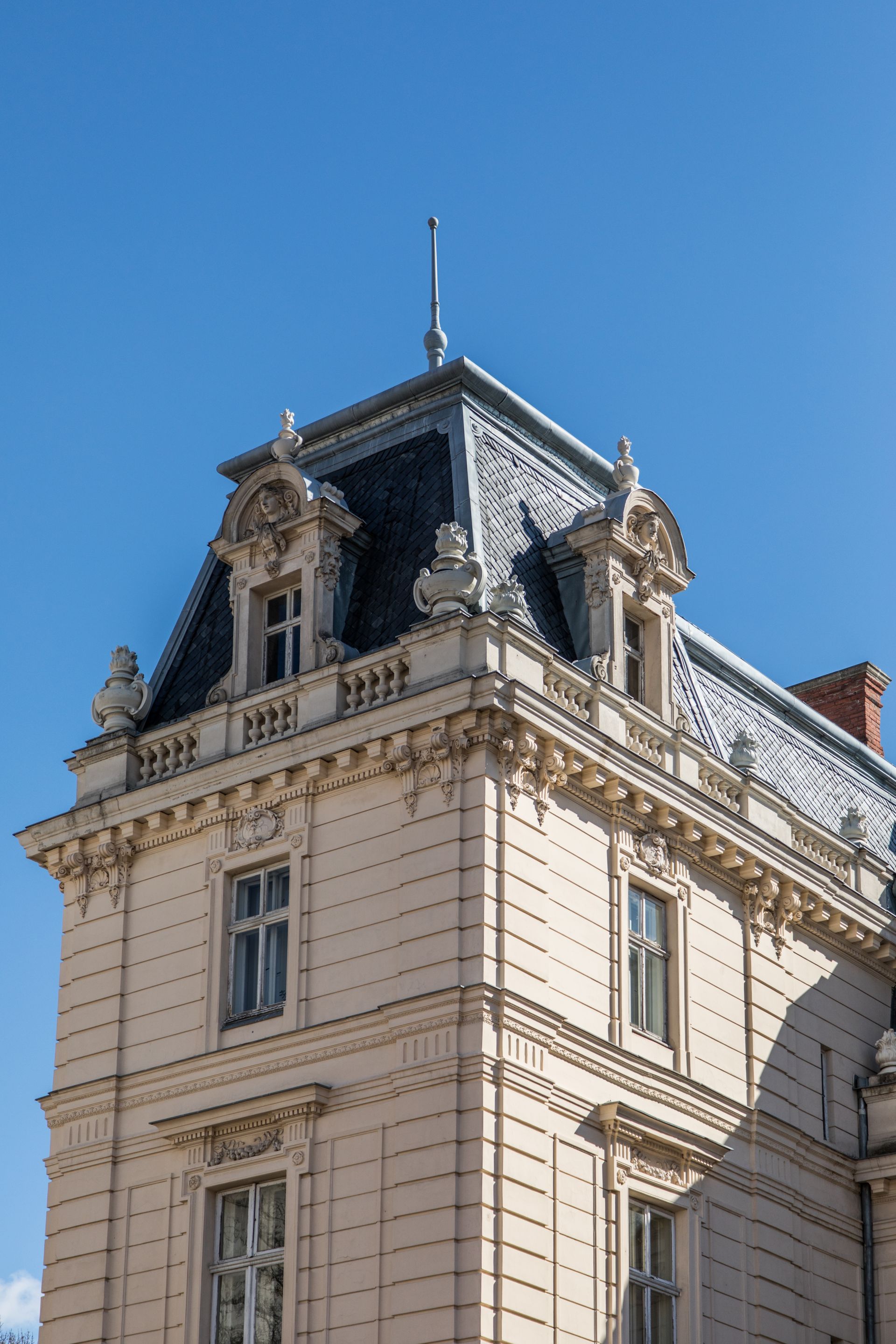 Bâtiment beige orné, coiffé d'un toit mansardé gris foncé, se détachant sur un ciel d'un bleu éclatant.
