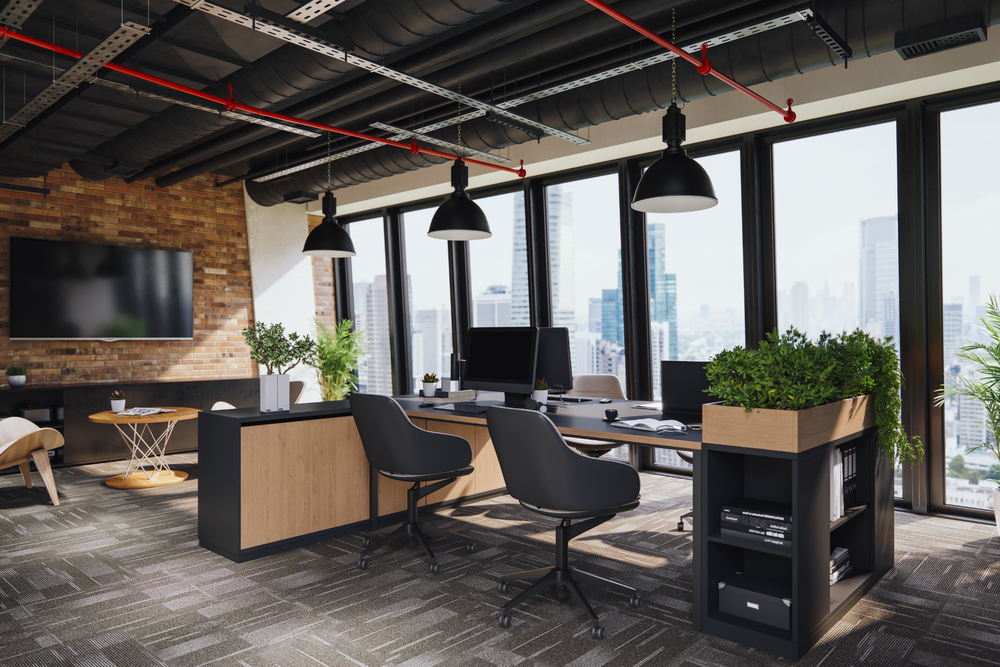 Modern office with workstations, plants, wood-paneled wall, flat-screen TV, and floor-to-ceiling windows overlooking a city.