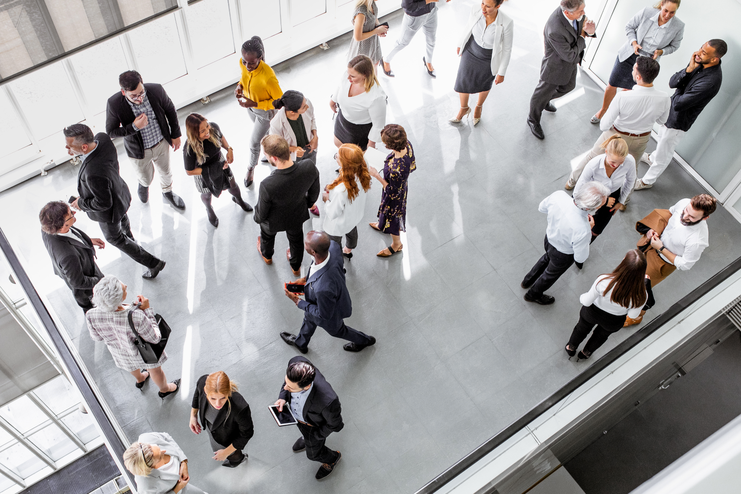 High-angle view of diverse professionals networking in a bright, modern office space with a polished concrete floor.