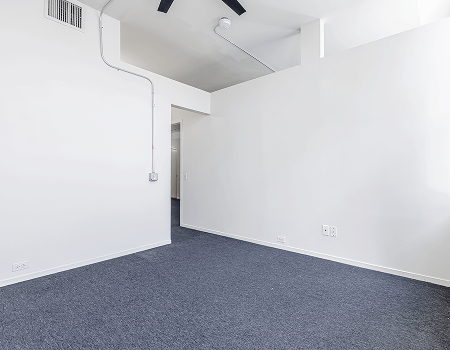 An empty room with a ceiling fan and a blue carpet.