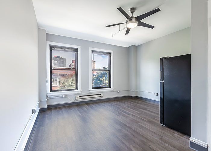 An empty room with a black refrigerator and a ceiling fan.