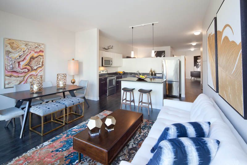 A living room with a couch , table and chairs and a kitchen in the background.