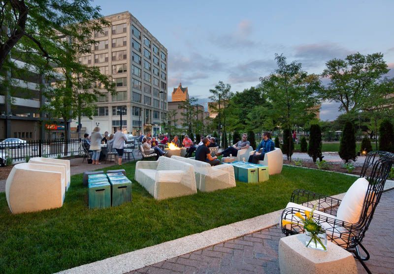 A group of people are sitting around a fire pit in a park.