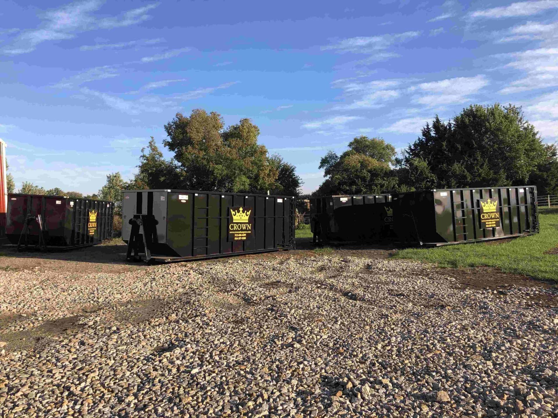 Dumpsters lined up on gravel under a blue sky, some with a yellow logo.