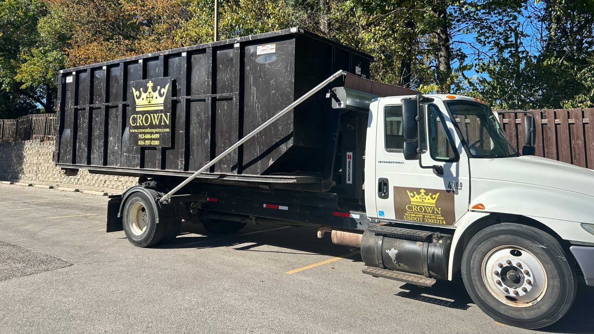 Dumpster truck with black container, logo on container and truck, parked on pavement.
