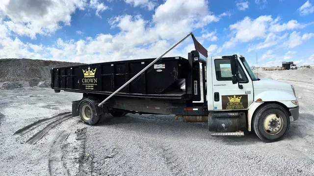 White Crown Dump truck on a gravel surface under a partly cloudy sky.