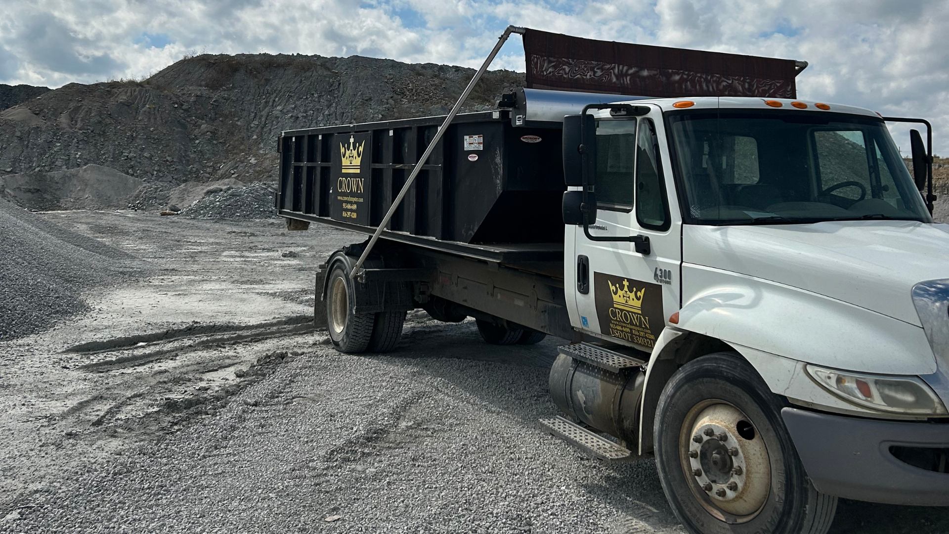 White dump truck on gravel in a quarry. Black bed with lettering, gray pile of rocks in background.