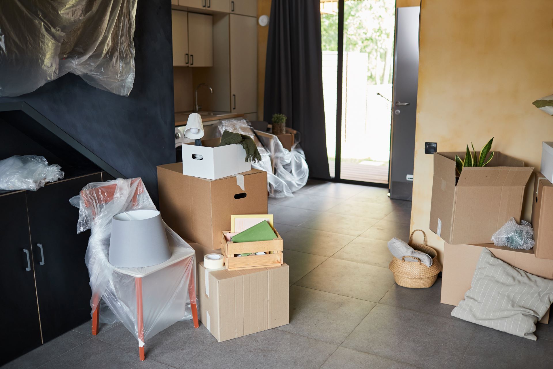 Unpacked moving boxes and household items in a room near a glass door.
