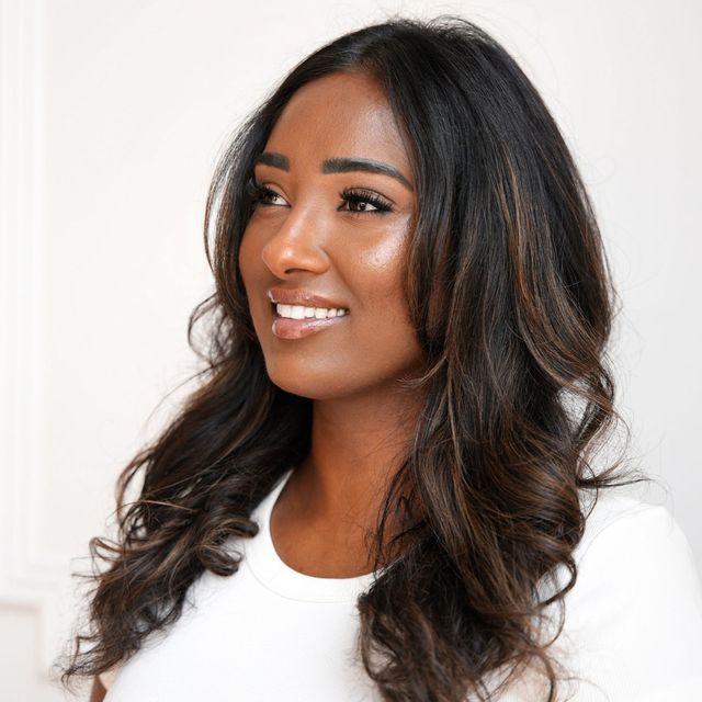 Woman with long, dark hair, smiling, wearing a white shirt, looking to the side.