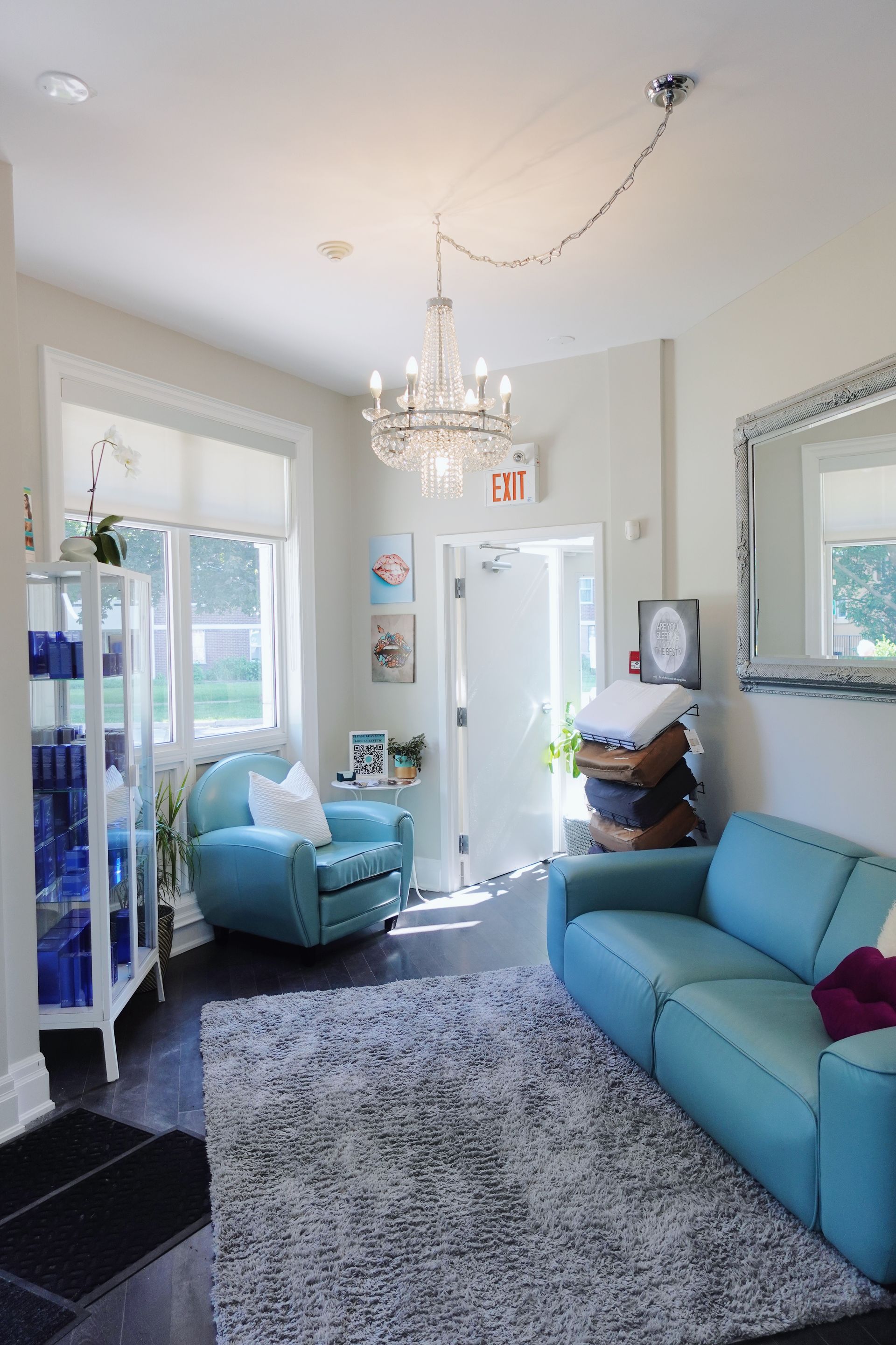 Waiting room with teal furniture, chandelier, and a white cabinet with blue bottles.