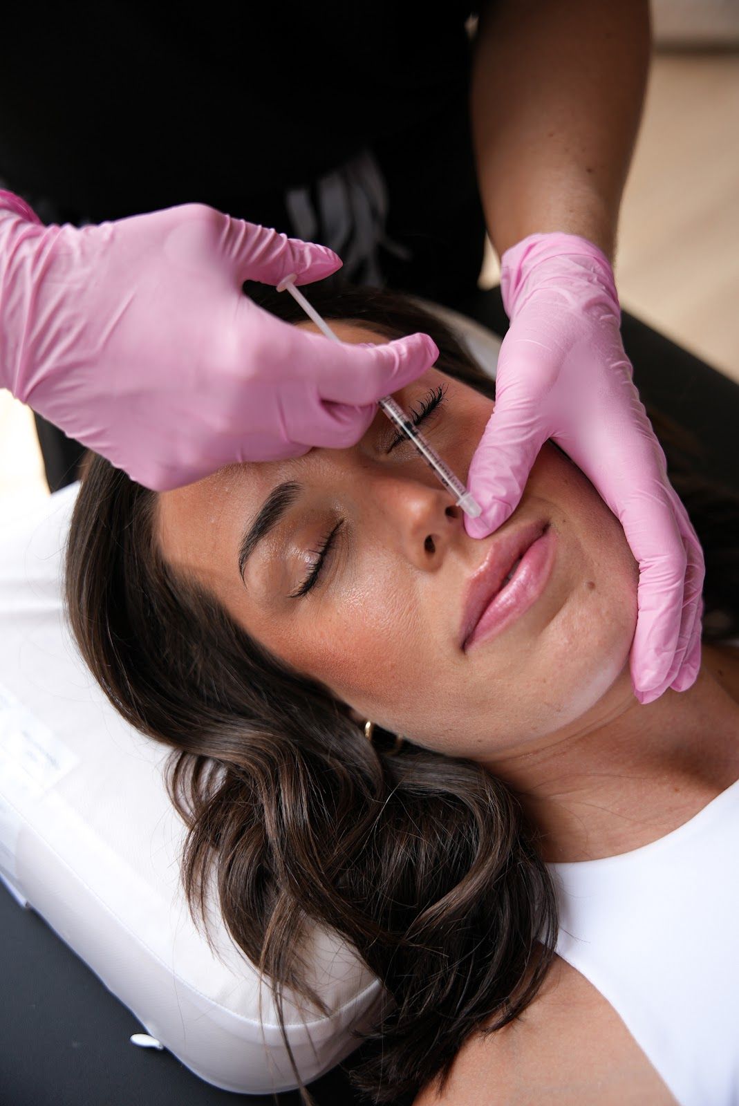 A practitioner in blue gloves uses a syringe to perform a dermal filler injection on a person’s upper lip.