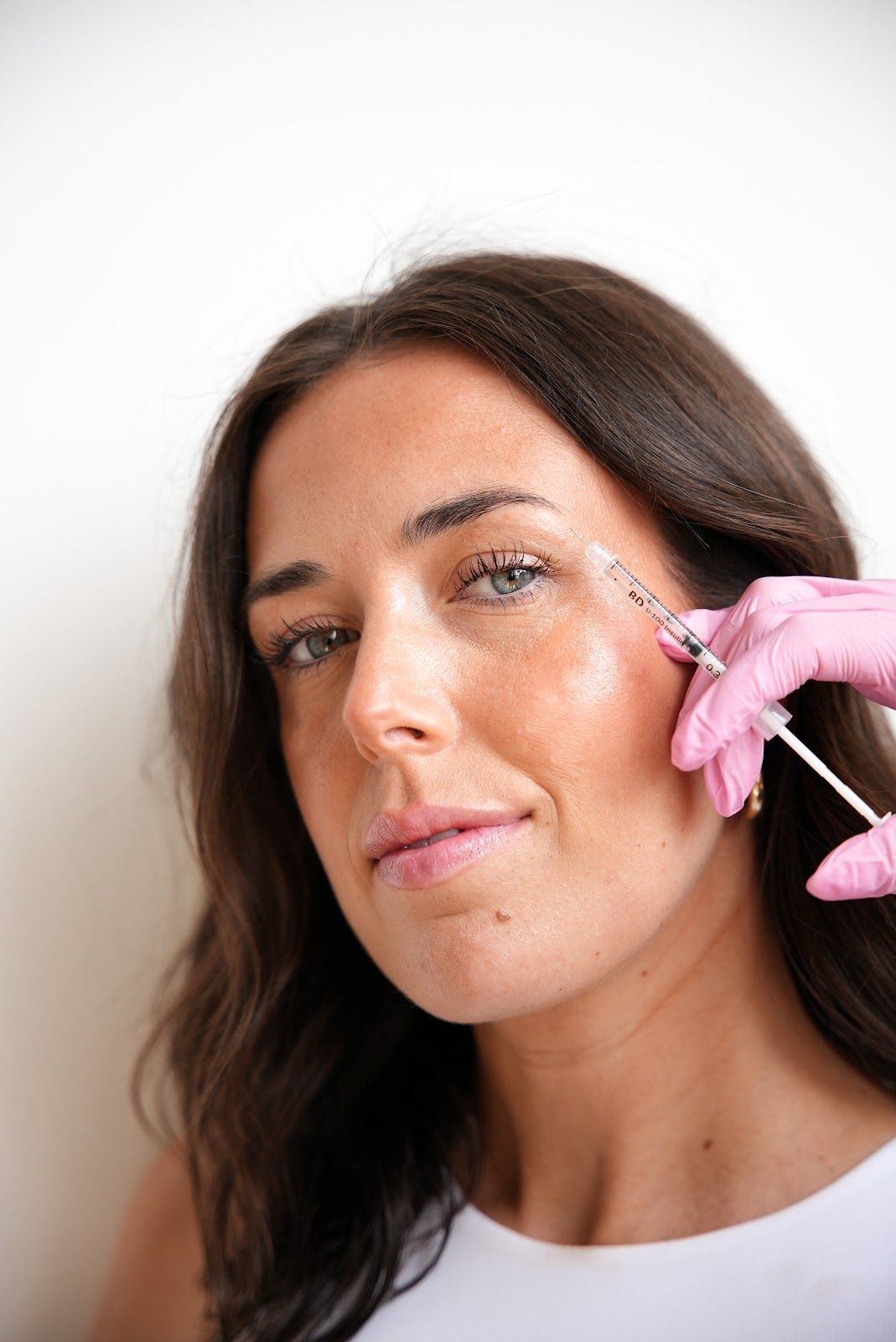 A technician uses tweezers to carefully apply lash extensions to a client lying down with an under-eye patch.