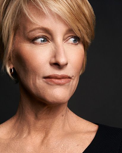 Blonde woman with short hair looking off to the side. She has a subtle smile and is wearing a black top.