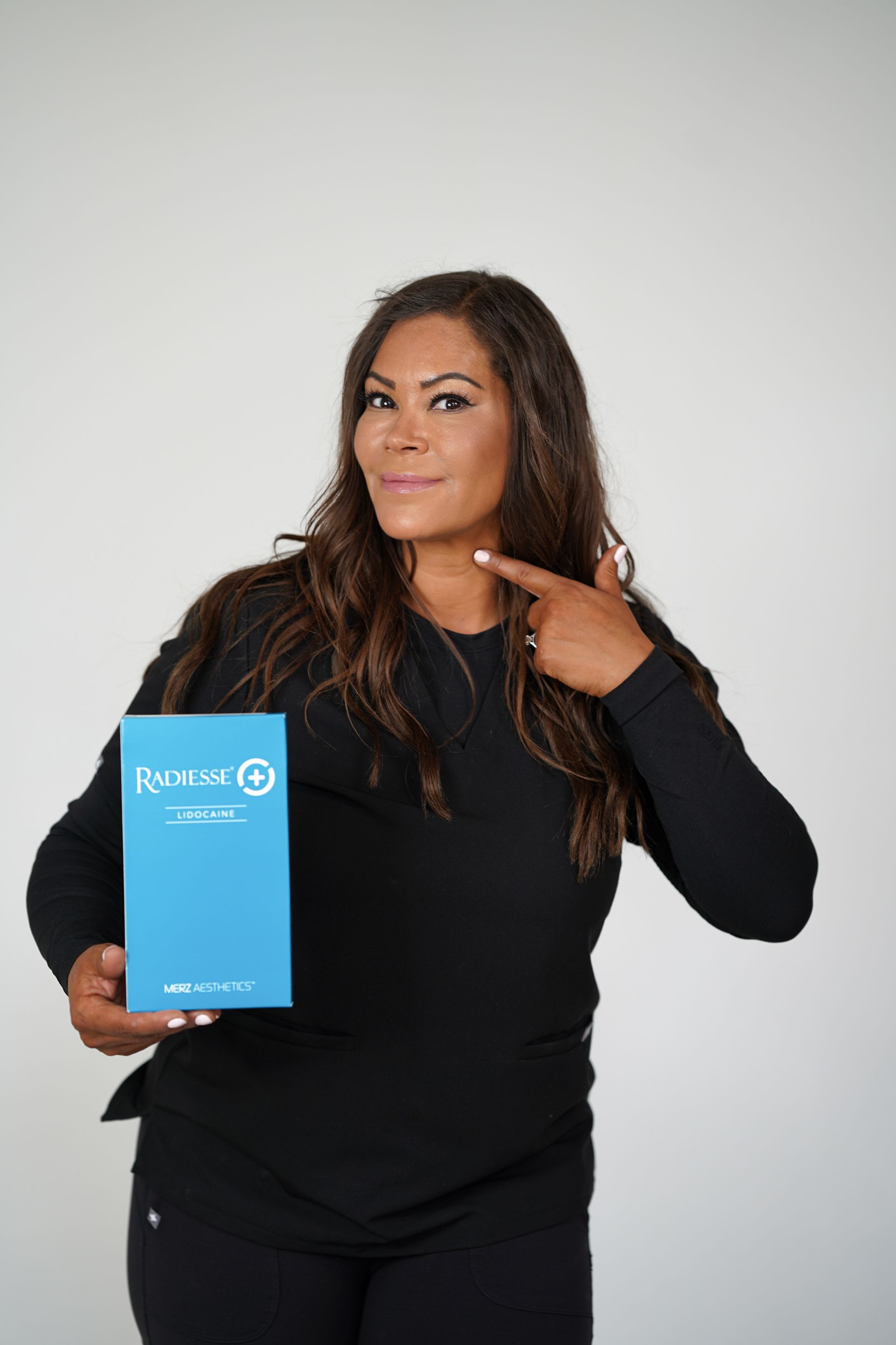 Woman in black holding a blue box and pointing to her neck against a white background
